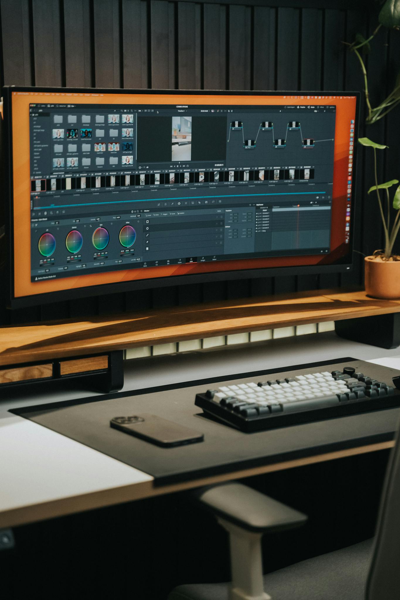 Sleek home office desk with ultrawide monitor for video editing, keyboard, and smartphone.